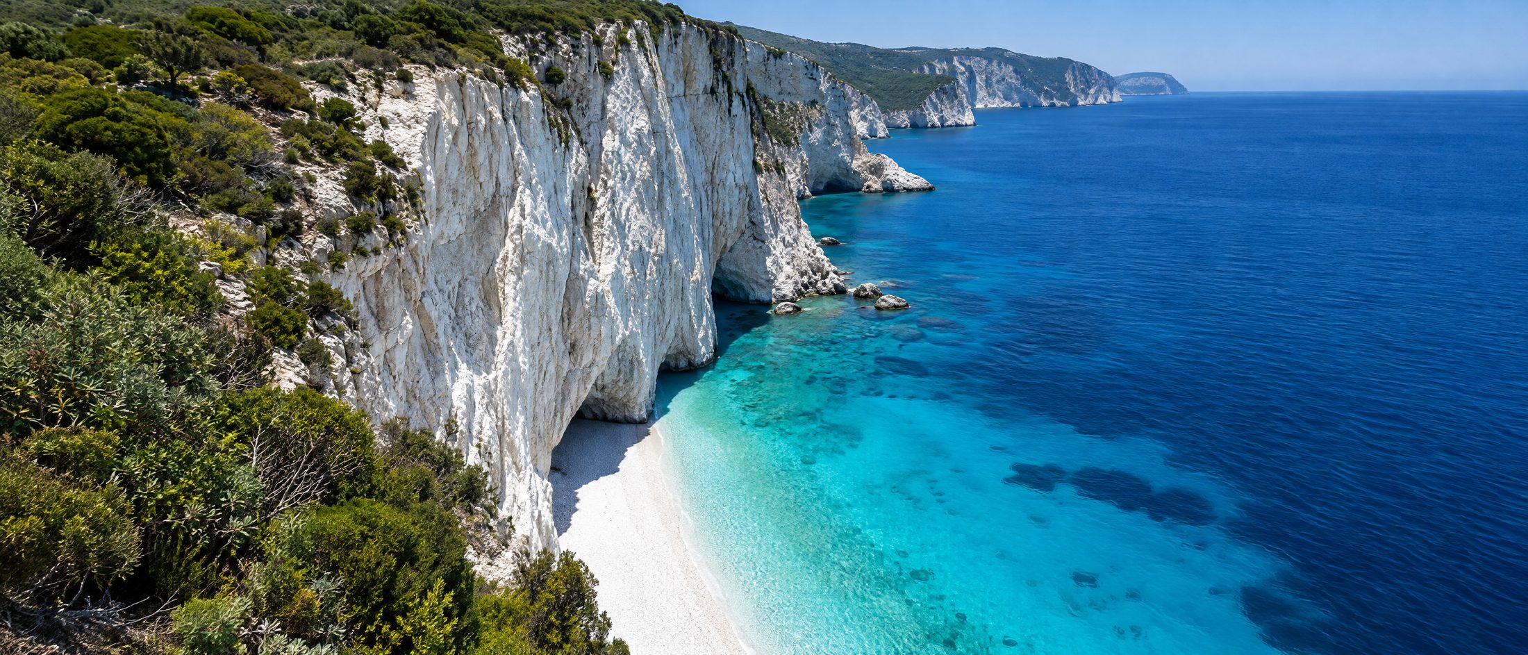 White limestone cliffs dropping into graduated turquoise above a narrow pebble beach